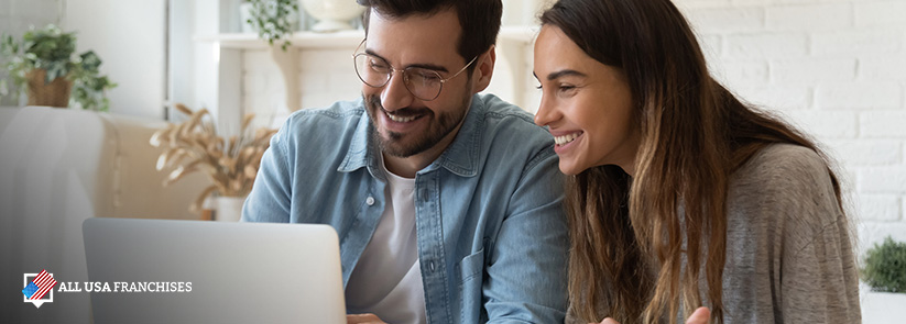 Couple Smiling Looking at the Benefits of Investing in a Franchise on a Laptop